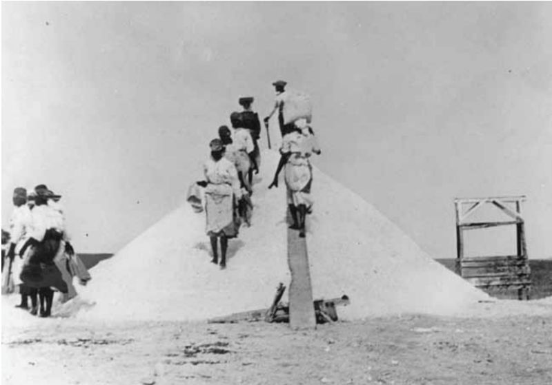 Historische foto: mensen lopen met manden langs een zoutberg
